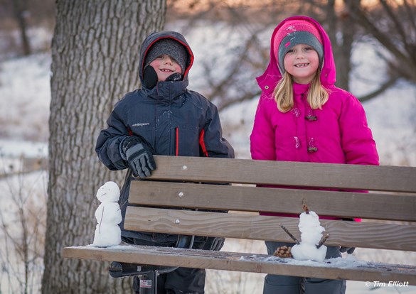 two young children playing in the snow, building snowman.