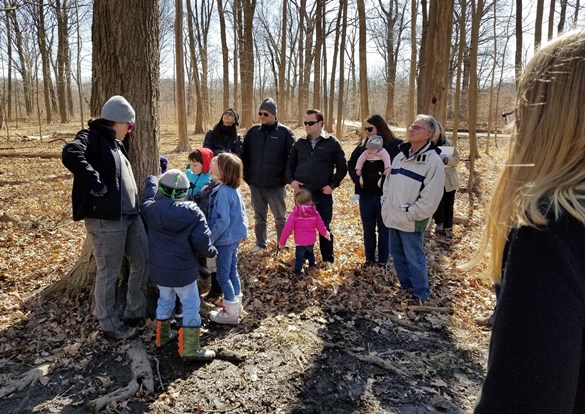 Instructor with a group of adults and children in the woods during a maple syrup hike.