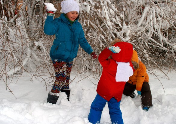 Three young children in bright colored snowsuits, playing in the snow