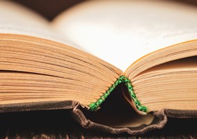 Close-up photo of old book binding, yellowed pages with green thread stitching