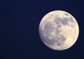 Brightly lit bluish gray full moon hanging in a dark blue sky.