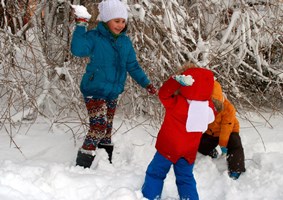 Three young children in bright colored snowsuits, playing in the snow