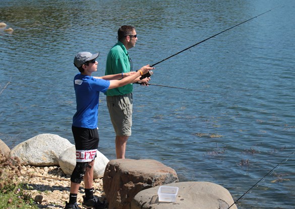 Educator teaching a young boy how to fish along a shoreline