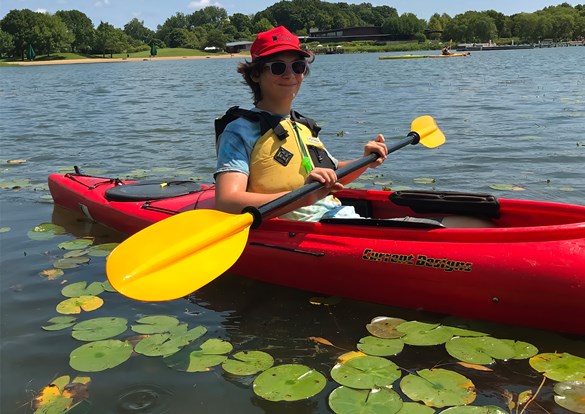 Young boy floating in a kayak in a pond filled with lilly pads.