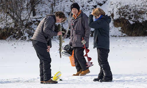 Three young men pulling a large fish from the their ice fishing hole