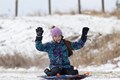 Young girl on a sledding raising her arms and hands in the air