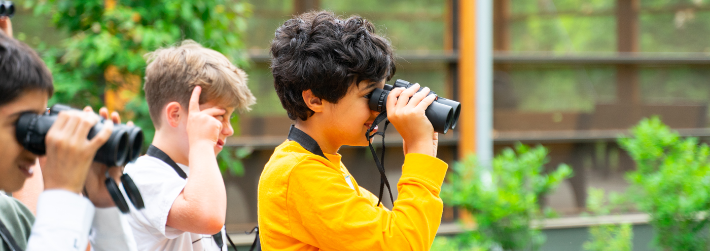 School students outdoors looking through binoculars