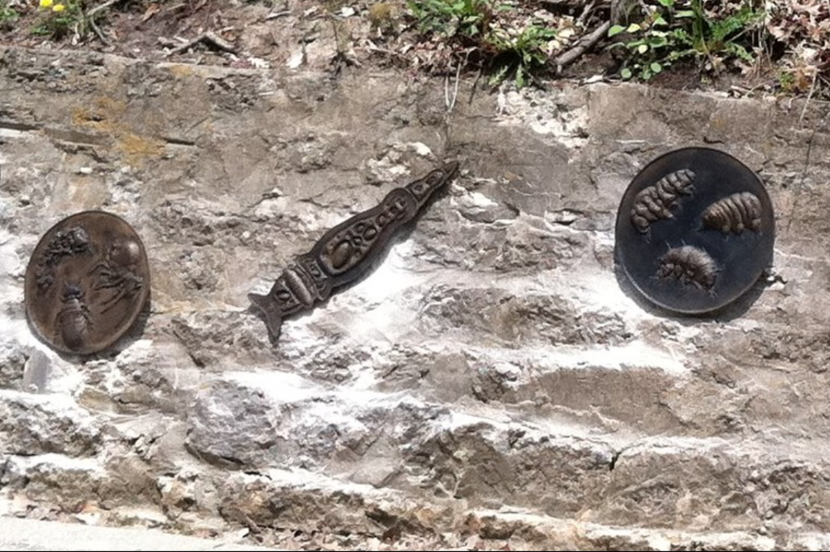 Sculptural bronze-look relief plaques affixed to a stone wall along the ravine path